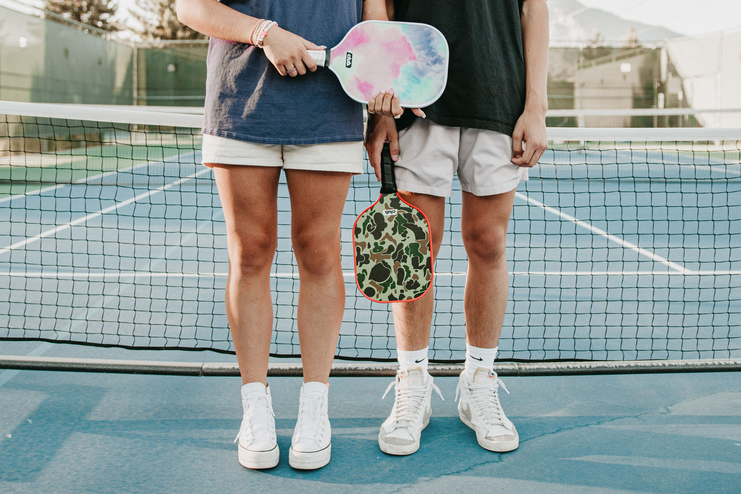 2 people hold pickleball paddles on a pickleball court