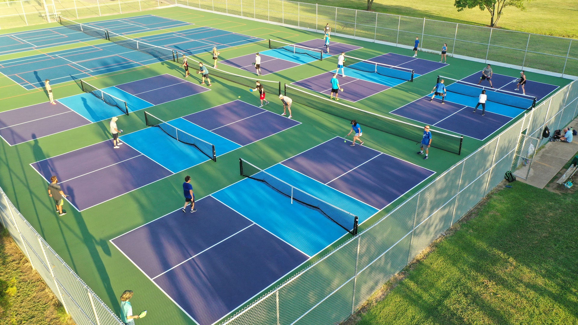 Beginners playing pickleball on 6 outdoor courts using graphite pickleball paddles 